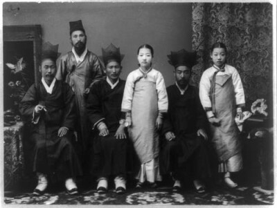 照片上的人身着传统朝鲜服饰,站在中间的女孩拿着一副眼镜.