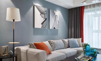 客厅整体以冷色为基调,舒适的布艺沙发搭配蓝灰色背景墙,一抹橘色的